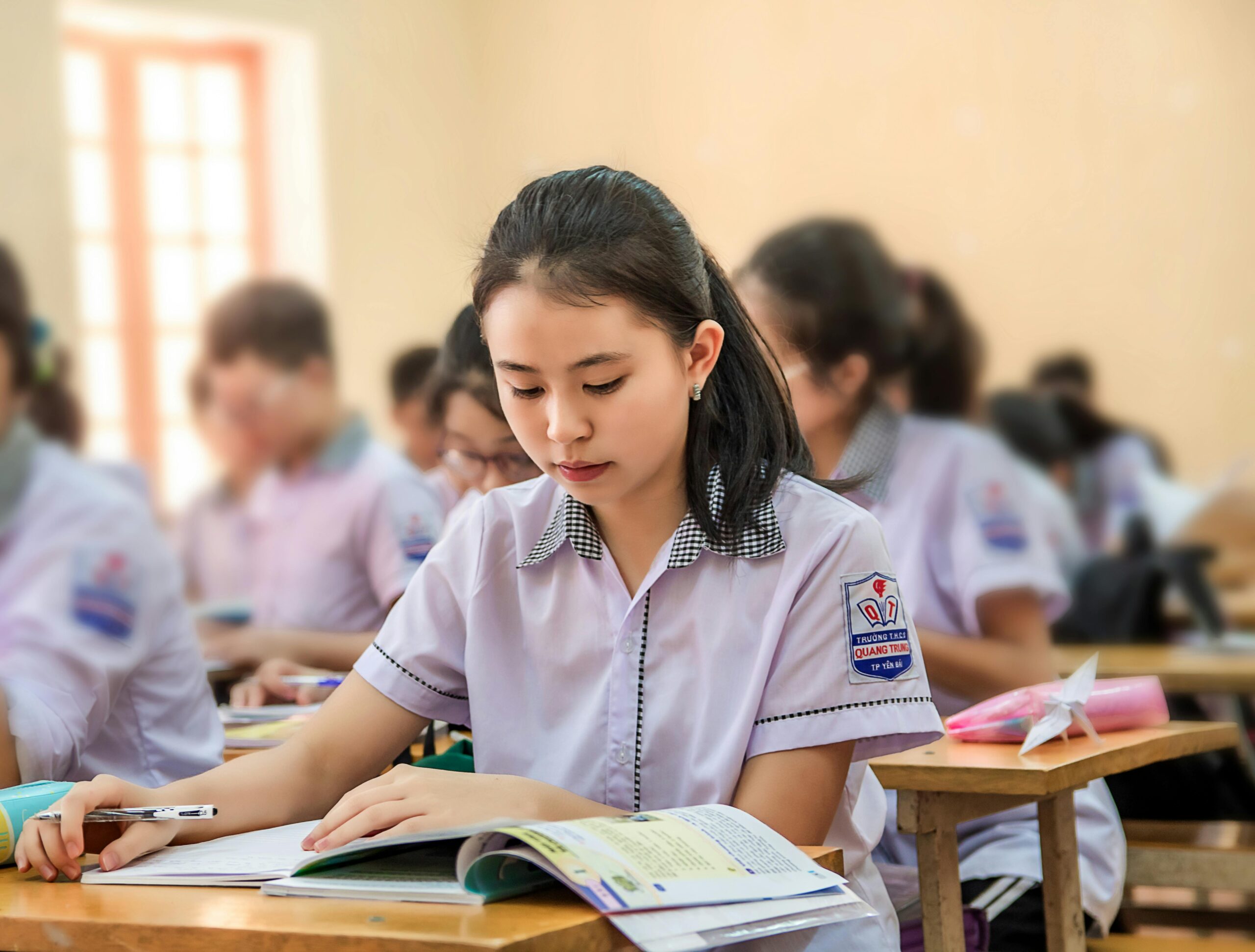 Young Asian student focusing on her studies in a school classroom with blurred background.