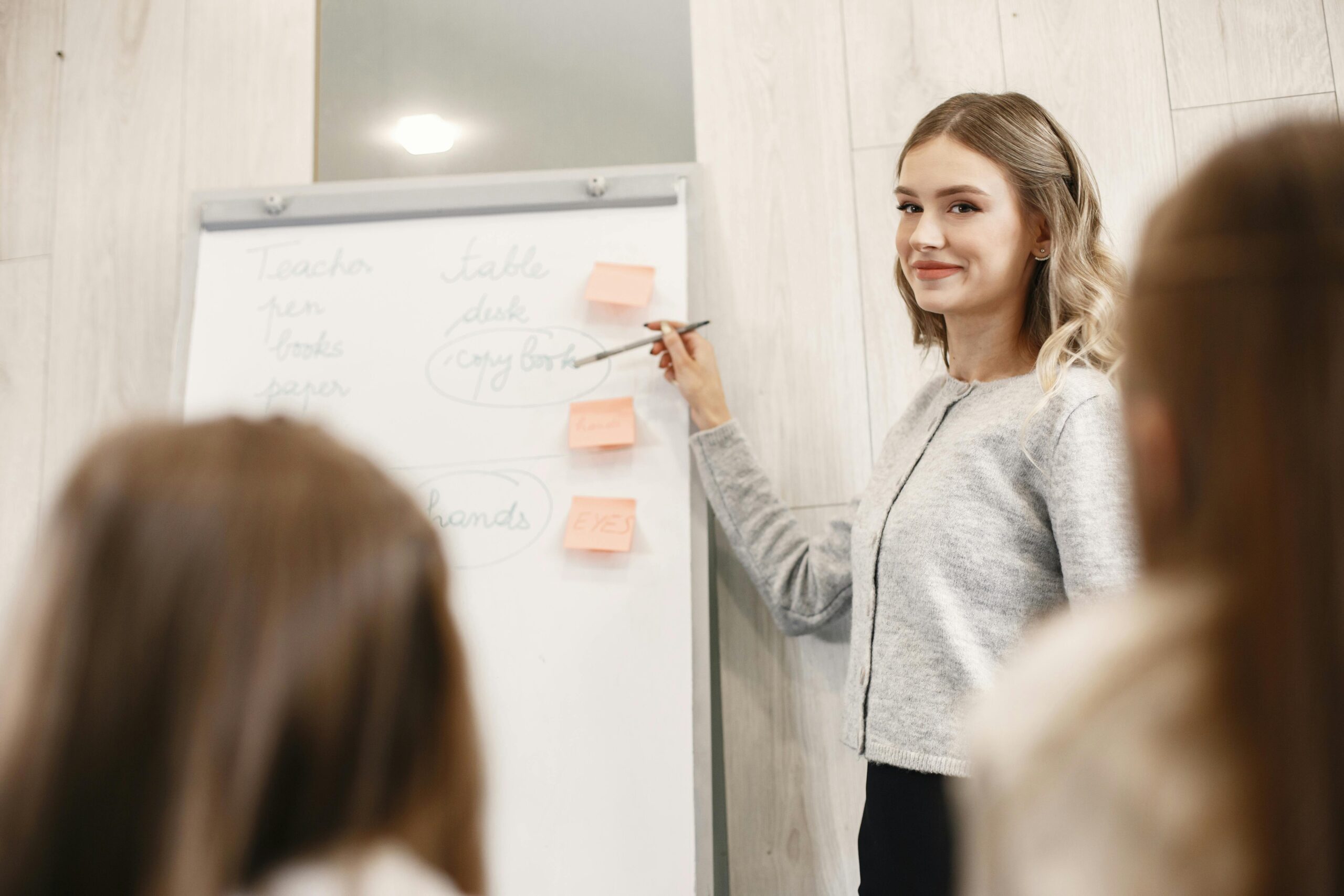 Female teacher smiling as she explains notes on a flipchart to a class.