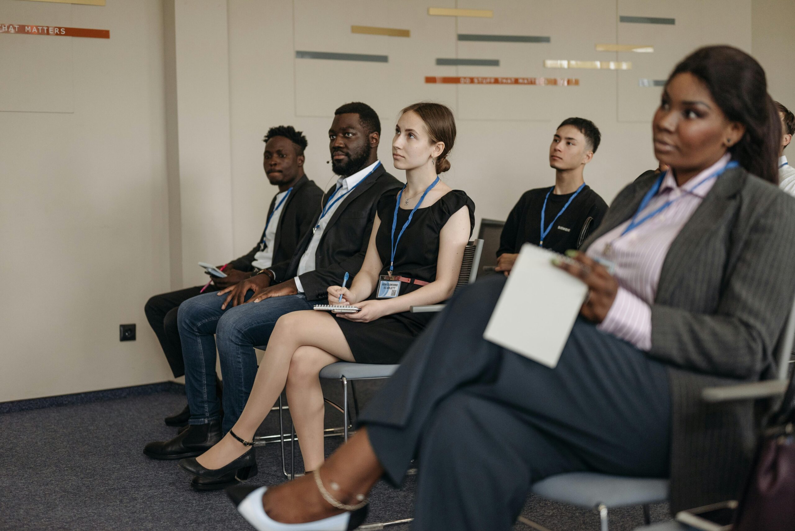 A diverse group of adults attentively listening in an indoor business meeting setting.